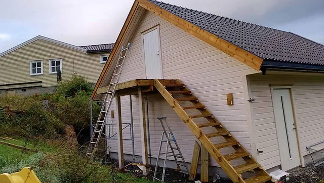 Garasje med utvendig trapp til loftsdør og byggestillas på siden.
