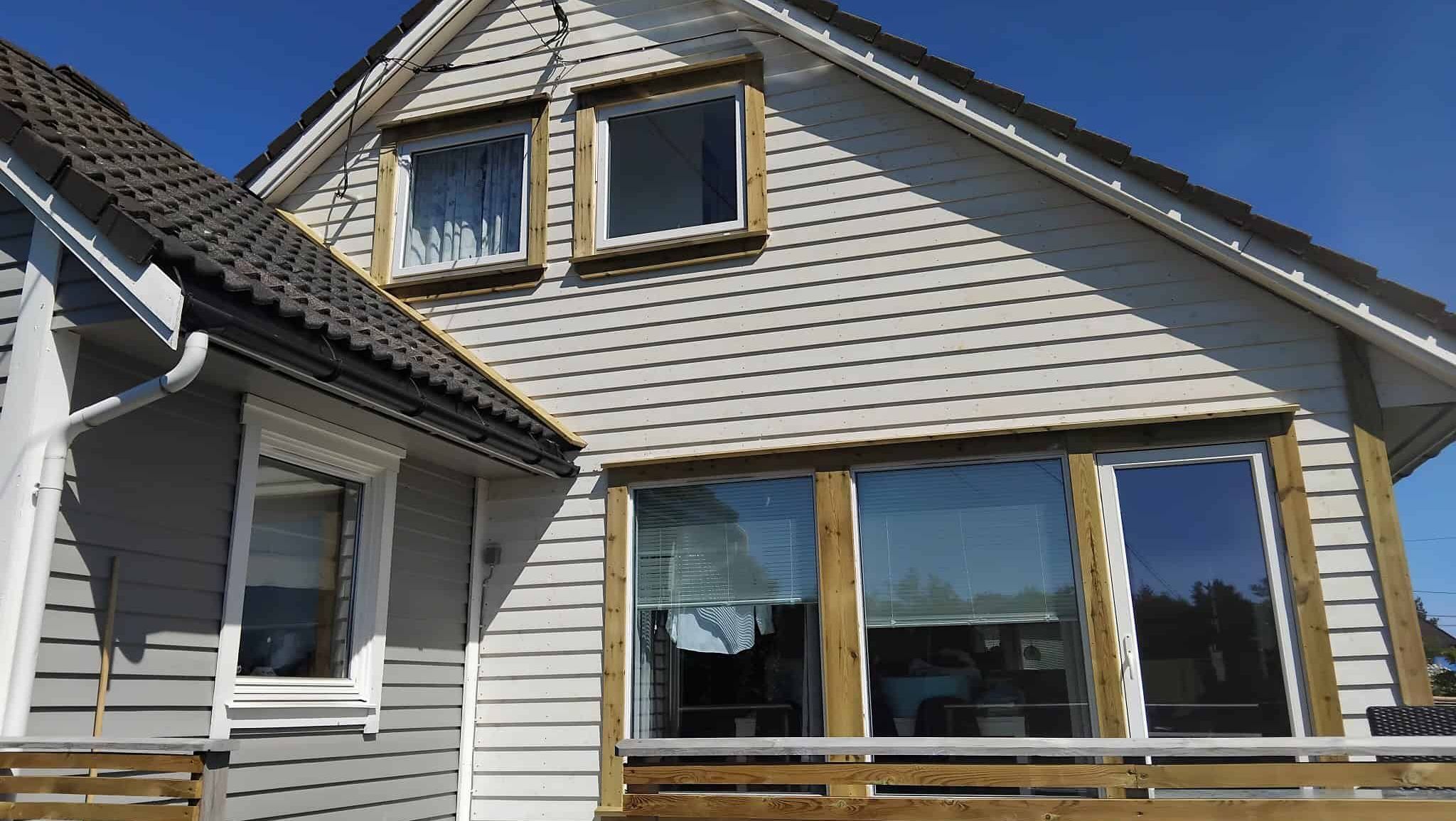 Hvit husfasade med nye vindusomramminger og mørkt tak mot klar himmel.