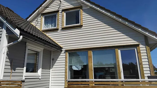 Hvit husfasade med nye vindusomramminger og mørkt tak mot klar himmel.